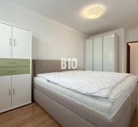 Világos szoba a nyaraló apartmanban ággyal, ruhásszekrényekkel és fa dekorációjú padlóval.