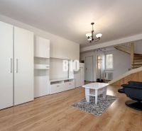 Nappali a nyaraló apartmanban fehér bútorokkal és fa mintás padlóval.
