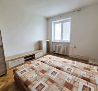 Szoba egy háromszobás lakásban, kétszemélyes ággyal és fa mintázatú padlóval.