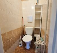 Fürdőszoba WC-vel, fehér csempékkel és polccal egy háromszobás lakásban.
