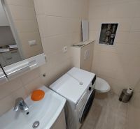 Fürdőszoba a garzonlakásban mosógéppel, mosdóval és WC-vel, világos falicsempékkel.