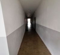 Hosszú folyosó fehér falakkal és csempézett padlóval egy egyszobás lakásban.