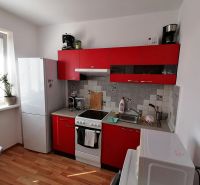 Konyha piros szekrényekkel és fa dekorációjú padlóval egy egyszobás lakásban.