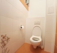 Fehér csempékkel és narancssárga padlólapokkal ellátott WC egy háromszobás lakásban.