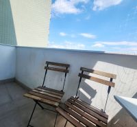 Egy 3 szobás lakás erkélye két fa székkel, kék éggel és védőhálóval.