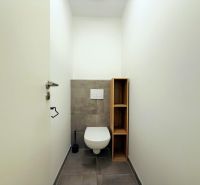 WC szürke csempével és fa polccal egy kétszobás lakásban.