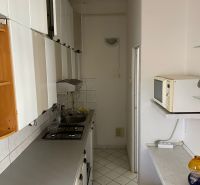 Keskeny konyha egy kétszobás lakásban fehér bútorokkal és csempékkel.