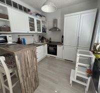 Konyha egy kétszobás lakásban fehér bútorokkal, bárpulttal és fa dekoros padlóval.