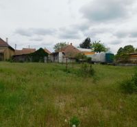 Pozemky na bývanie v Dvoroch nad Žitavou s vidieckymi stavbami a hustou trávou.