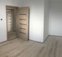 Szoba egy háromszobás lakásban, fa dekoros padlóval és világos falakkal.