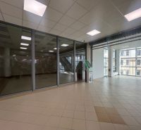 Üvegfalú üzlethelyiségek csempével és bankautomatával, belső tér nagy ablakokkal.