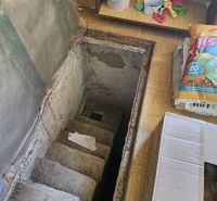 Betonlépcsők a pincébe vezető házikóban, körülvéve tárolt tárgyakkal.