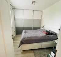Hálószoba egy háromszobás lakásban, fa mintázatú padlóval és nagy szekrénnyel.