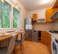 Két szobás lakás konyhája fa dekorációval és készülékekkel, gyönyörűen megvilágítva.