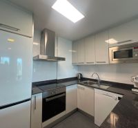 Konyha üdülő apartmanban fehér szekrényekkel, készülékekkel és fekete munkalappal.