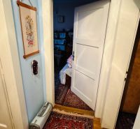 Szoba egy háromszobás lakásban szőnyeggel és nyitott ajtókkal, fa dekoros padlóval.