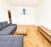 Nappali egy kétszobás lakásban, fa mintázatú padlóval és szürke kanapéval.