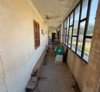 Keskeny folyosó egy családi ház verandáján régi ablakokkal és repedezett falakkal.