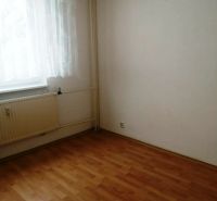 Szoba egy háromszobás lakásban fa dekoros padlóval, függönnyel és radiátorral.