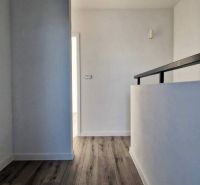 Folyosó egy családi házban, fa dekoros padlóval és fehér falakkal.