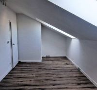 Tetőtér egy családi házban fa mintázatú padlóval és tetőablakkal.