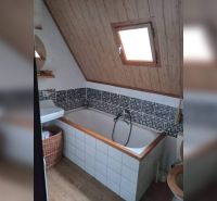 Fürdőszoba káddal és ferde mennyezettel, fa dekoráció, mozaik csempe, ablak.