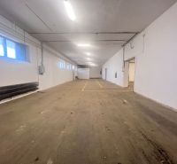 Raktár belső betonpadlóval és fehér falakkal, fénycsöves világítással.
