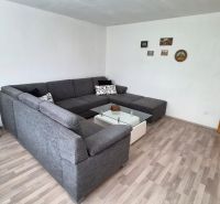 Nappali sarokkanapéval, üvegasztallal és fa mintázatú padlóval.