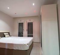 Rekreační apartman hálószobája nagy ággyal, fehér és szürke falakkal.