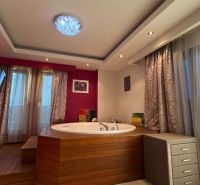 Nyaraló apartman pezsgőfürdővel, fa hatású padlóval, rózsaszín falakkal, televízióval, függönyökkel.