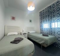 Rekreációs apartman két egyszemélyes ággyal, mintás függönyökkel és asztallal lámpával.