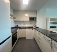 A nyaraló apartman konyhája fényes szekrényekkel és sötét munkalappal.