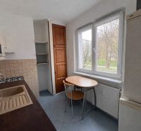 Konyha egy kétszobás lakásban fa szekrényekkel és asztallal az ablak mellett.