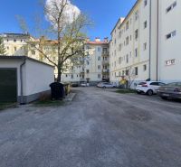 Lakóház melletti parkoló Besztercebányán autókkal és fákkal.