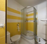 Fürdőszoba WC-vel és zuhanyzóval egy egyszobás lakásban, sárga csempékkel.