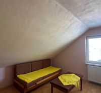 Tetőtéri szoba családi házban, ablakkal és ággyal, fa dekorációjú padlóval.