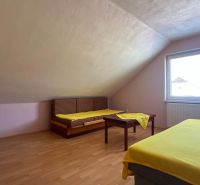 Világos tetőtéri szoba két ággyal, asztallal és fa dekorációjú padlóval.