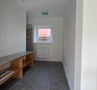Keskeny tér ablakkal, radiátorral, polcokkal és szürke padlóval egy családi házban.