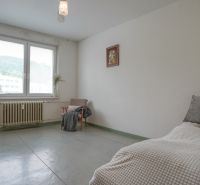 Hálószoba egy kétszobás lakásban nagy ablakkal, székkel és egyszerű berendezéssel.