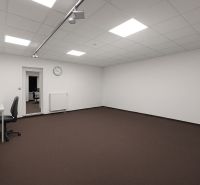 Priestranné Kancelárie s bielymi stenami, hnedým kobercom a minimalistickým zariadením.