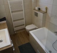 Fürdőszoba egy kétszobás lakásban káddal, mosdóval és fa dekorációjú padlóval.