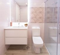 Fürdőszoba a nyaraló apartmanban fa mintázatú padlóval és zuhanyzóval.