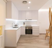 Konyha a nyaraló apartmanban fehér szekrényekkel és fa hatású padlóval.
