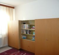 Szoba egy kétszobás lakásban könyvespolccal és nagy szekrénnyel, fa dekoros padlóval.