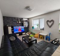 Nappali egy háromszobás lakásban kanapéval és TV-vel, fa dekorációjú padlóval.