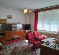 Nappali egy családi házban piros fotelekkel és üvegvitrinnel, fa dekoros padlóval.