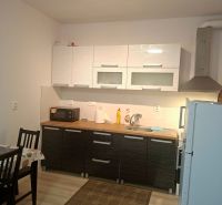 Konyhapult a garzonlakásban szekrényekkel, étkezőasztal, fa dekorációjú padló.