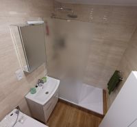 Fürdőszoba egy háromszobás lakásban WC-vel, zuhanyzóval és fa mintázatú padlóval.