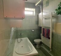 Fürdőszoba egy háromszobás lakásban káddal, zöld csempékkel, törölközőradiátorral.