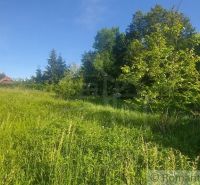 Zöld lakótelek Podkylaván, fákkal és kék éggel körülvéve.